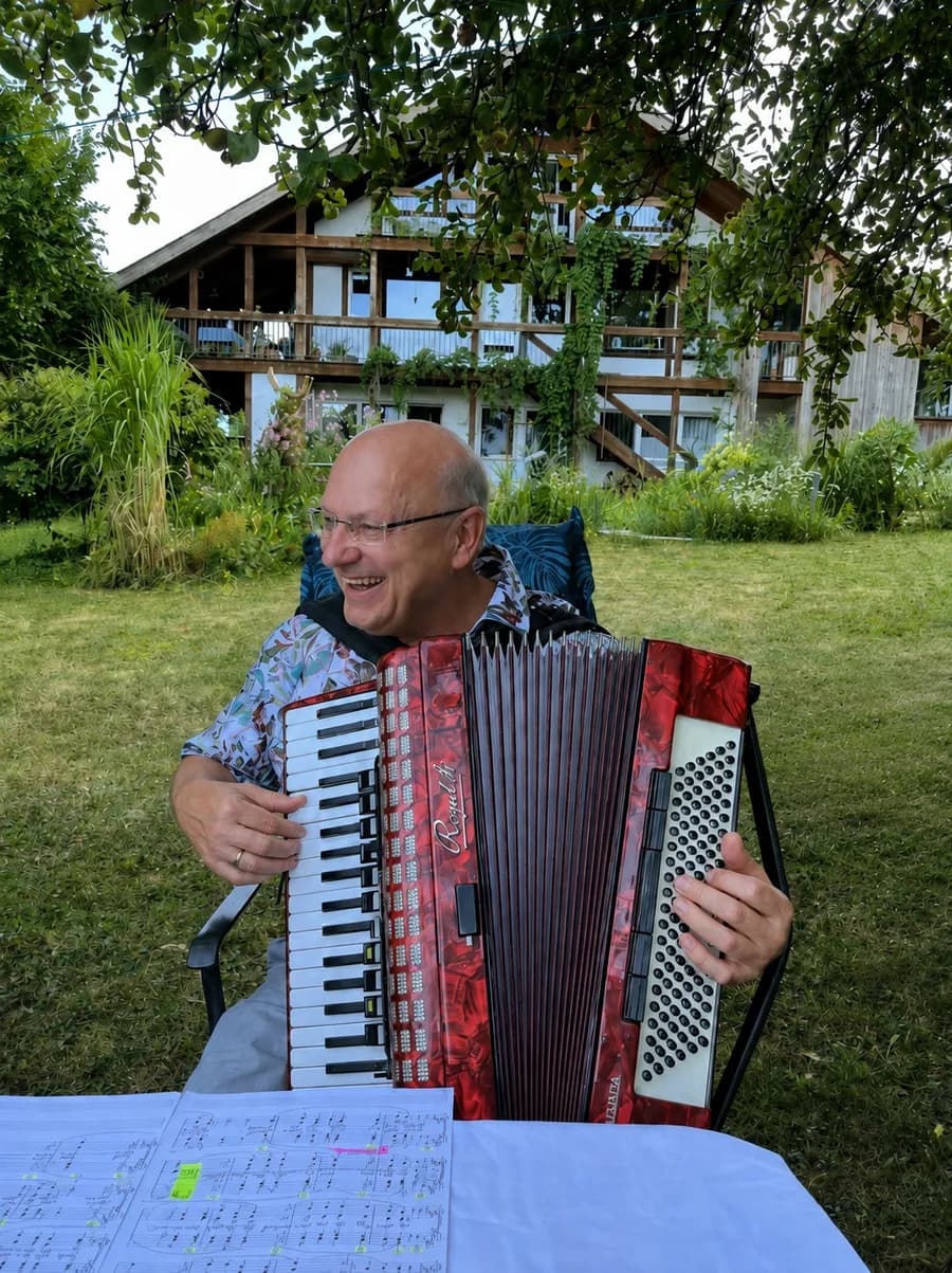 Josef Weimert spielt lachend Akkordeon in einem Garten