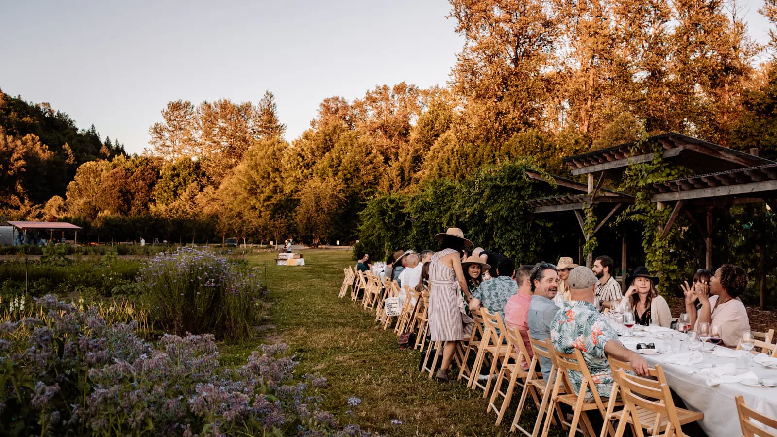 Lange Festtafel im Freien, an der Gäste im Abendlicht beisammensitzen